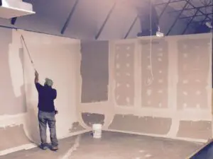 A man painting the wall of an unfinished room.